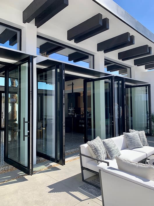 Elegant matte black double-leaf aluminum pivot doors by SPI Finestra open up to the patio in this Palm Springs Villa